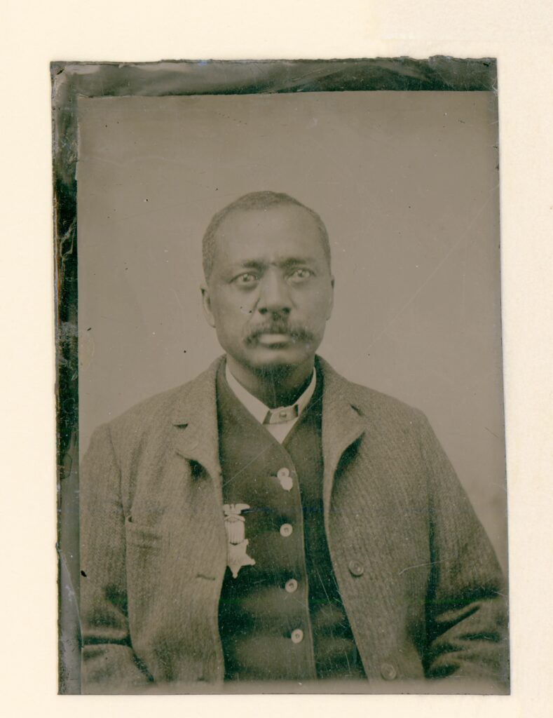A Civil War veteran sitting wearing a coat over a vest and on the vest is a military medal.