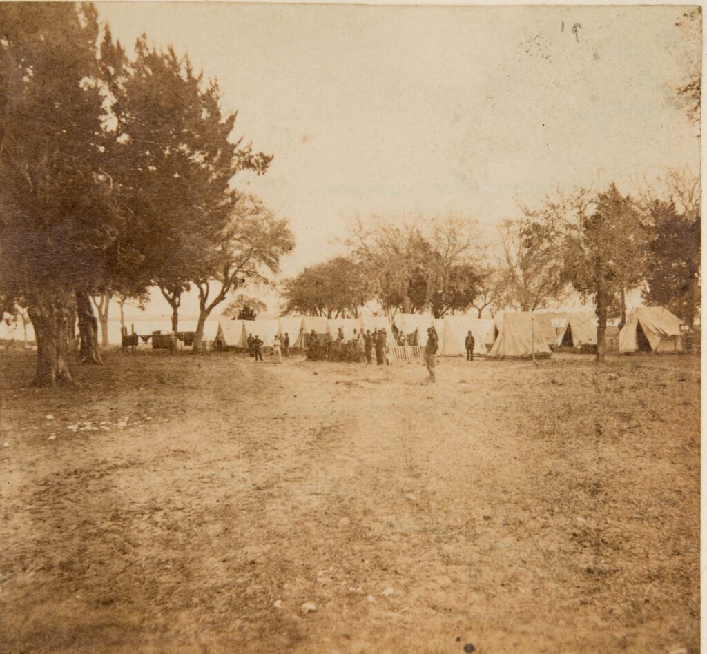 Military camp with soldiers standing outside of their tents in the distance.