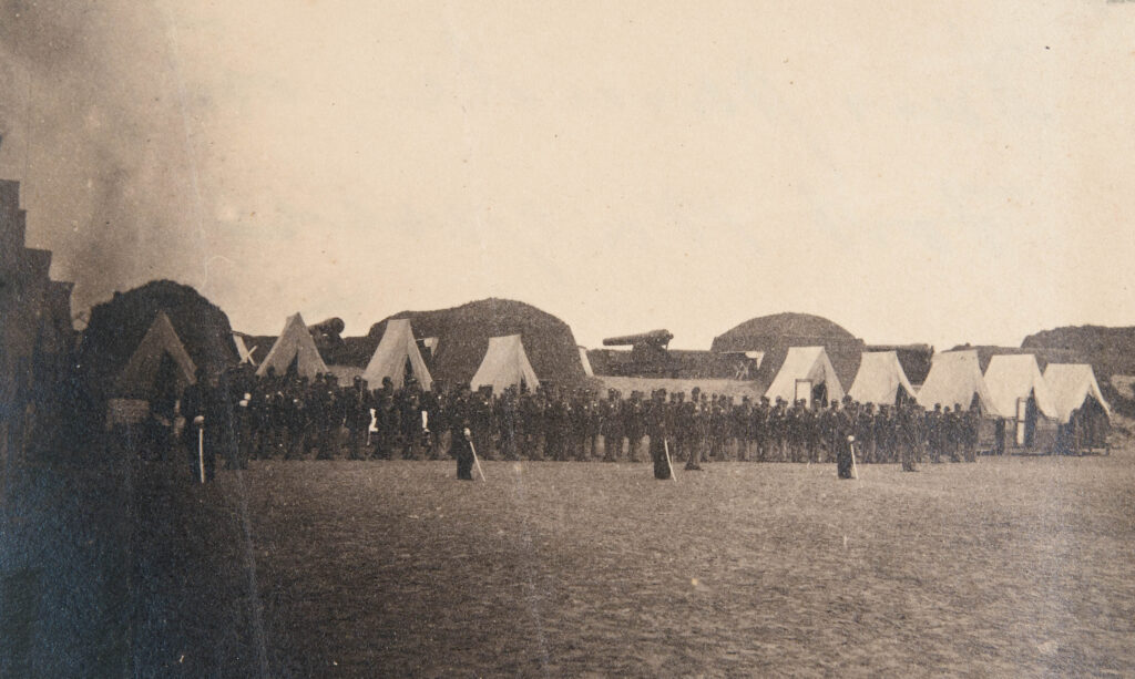 Military camp with soldiers lined up and tents behind them.